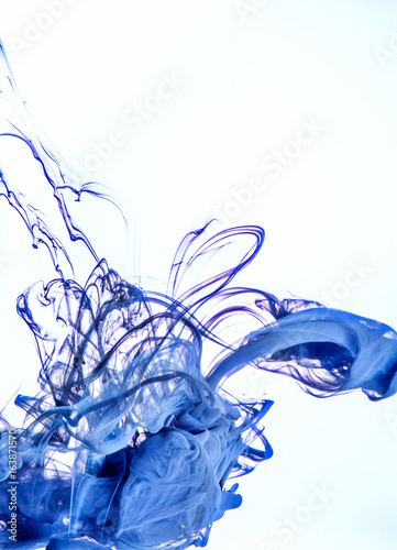 Ink swirl in a water on white background. The paint in the water. Soft dissemination a droplets of colored ink in water close-up. Explosion of color splashes acrylic ink.