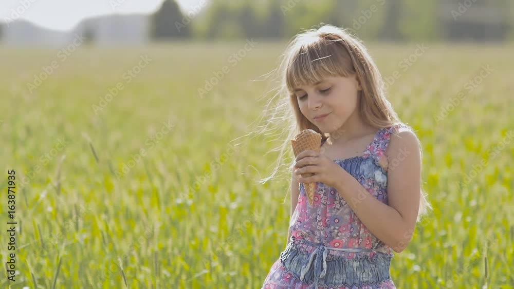 Beautiful blond little girl eats ice-cream in the summer next to the wheat field. Warm sunny day. Beautiful blond little girl eats ice-cream in the summer next to the wheat field. Warm sunny day.