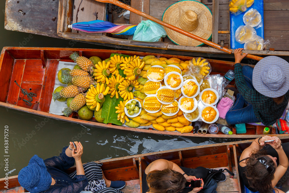 Obraz premium Traveler enjoying and take a photo with smartphone on long trail boat at Damnoen Saduak floating market in Ratchaburi near Bangkok, Thailand