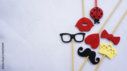 Top or flat lay view of Photo booth props a black mustache a black glases, a red bow tie, a ladybird, a red heart shape, a red lips and a yellow crown on a white isolated background flat lay. Birthday