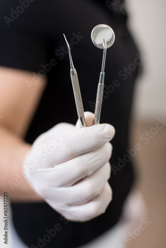 Male dentist with white gloves holding dental equipment - mirror and probe at the dental office. Close-up, selective focus on tools. Dentistry