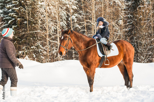 Small girl, horse trainer and horse in a winter