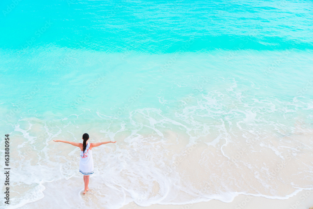 Young happy tourist girl at beach having a lot of fun in shallow water. Top view of a young girl and a snow-white beach with turquoise clean water.