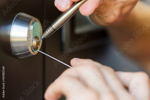 closeup of locksmith hands using pick tools to open locked door photo