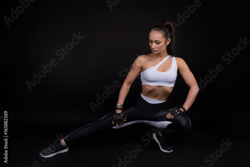 Portrait of fitness athletic young woman. Female model with muscular body in sports clothing. Studio shot with copy space on black background.