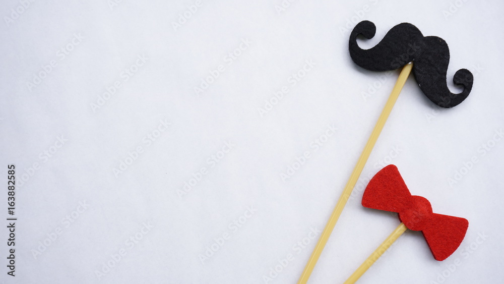 Top or flat lay view of Photo booth props red bow tie and a black mustache on a white background flat lay. Birthday parties and weddings. Top or flat lay view of Photo booth props red bow tie and a black mustache on a white background flat lay. Birthday parties and weddings.
