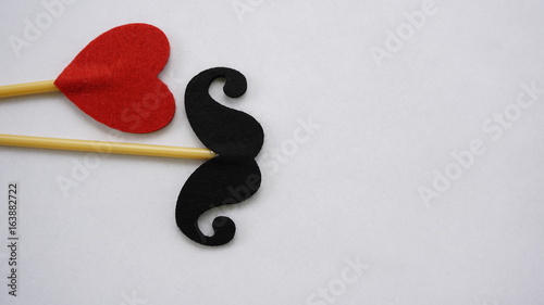 Top or flat lay view of Photo booth props red heart shape and a black mustache on a white background flat lay. Birthday parties and weddings.