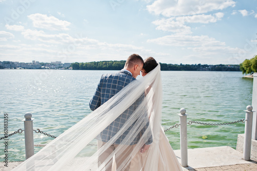 Stunning wedding couple walking on lakeside on a sunny day. © AS Photo Family