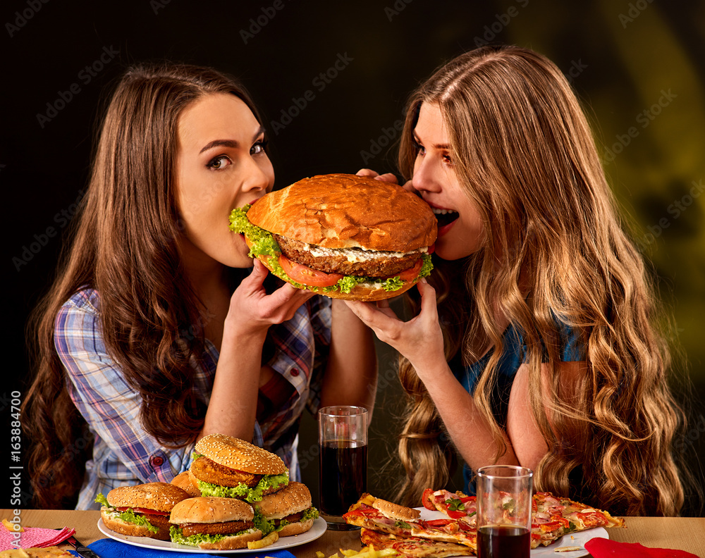 Women eating fast food. Gils eat hamburger with ham. Two female bite burder  junk from two