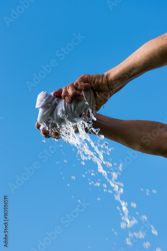 Fotografie Squeezing of wet cloth against blue sky.