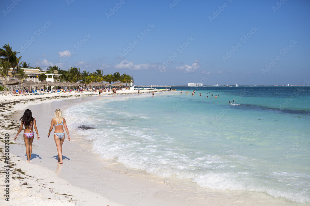 Sexy ladies walking on the beach wearing bikinis. White sand beach and turquoise sea. Focus point on the ladies on left. Vacation concept image.