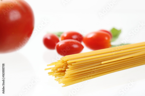 Raw spaghetti noodle with tomatoes and basil isolated in white background