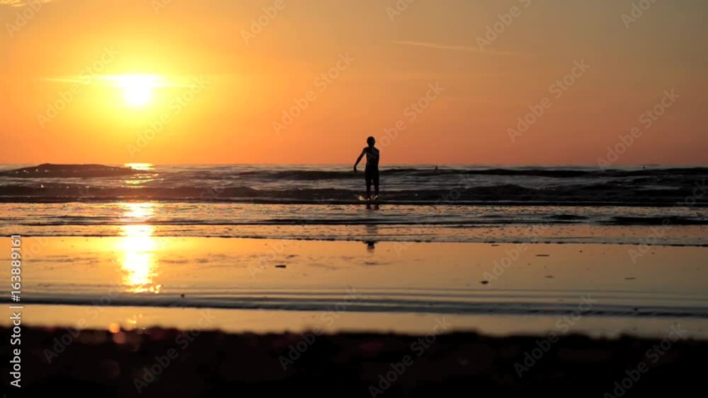 Silhouette of a kid walking and playing on beach at sunset
