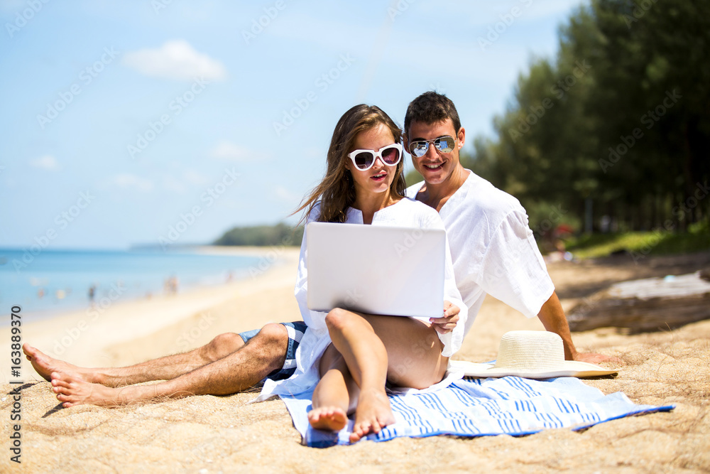 A couple playing laptop happily on beautiful beach in summertime