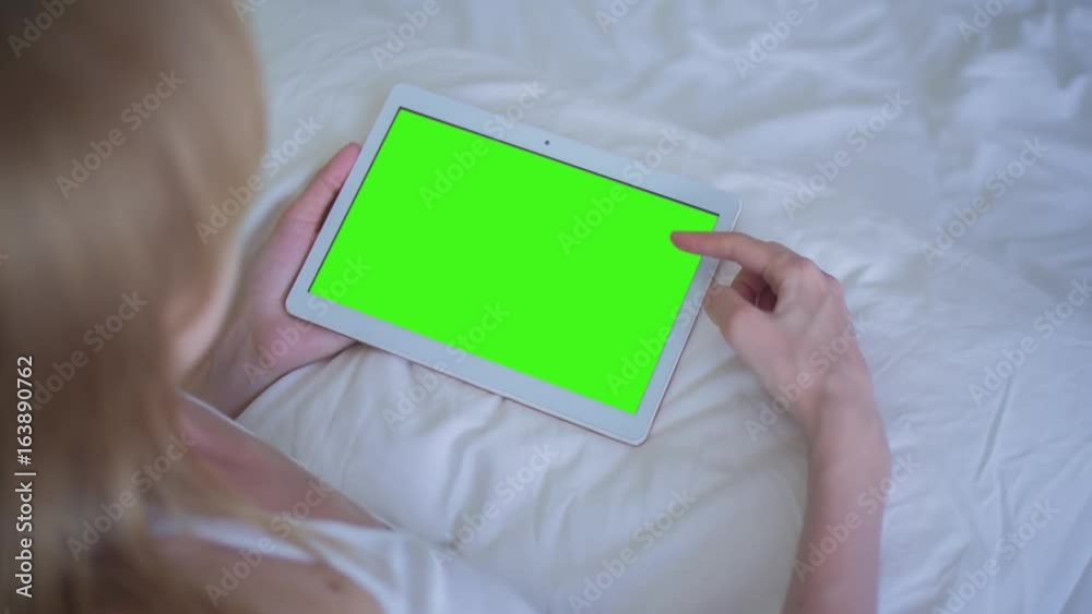 Young Woman in white top laying on bed uses Tablet PC with pre-keyed green screen. Few types of gestures - scrolling up and down, tapping, zoom in and out. Perfect for screen compositing Young Woman in white top laying on bed uses Tablet PC with pre-keyed green screen. Few types of gestures - scrolling up and down, tapping, zoom in and out. Perfect for screen compositing