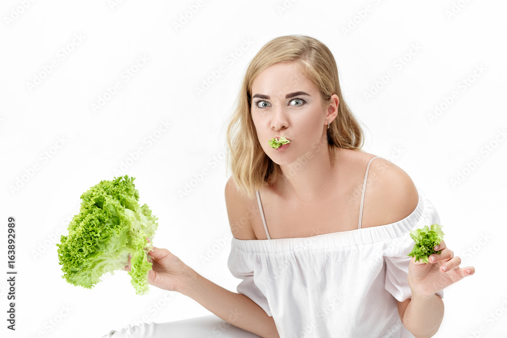 Beautiful blond woman in white blouse eating fresh green salad on white background. Health and Diet Beautiful blond woman in white blouse eating fresh green salad on white background. Health and Diet
