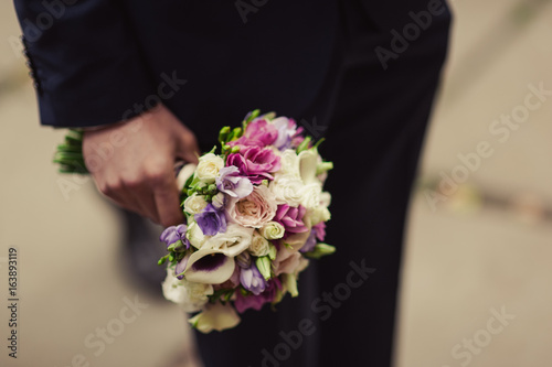 Wedding groom with bride's bouquet of flowers outside