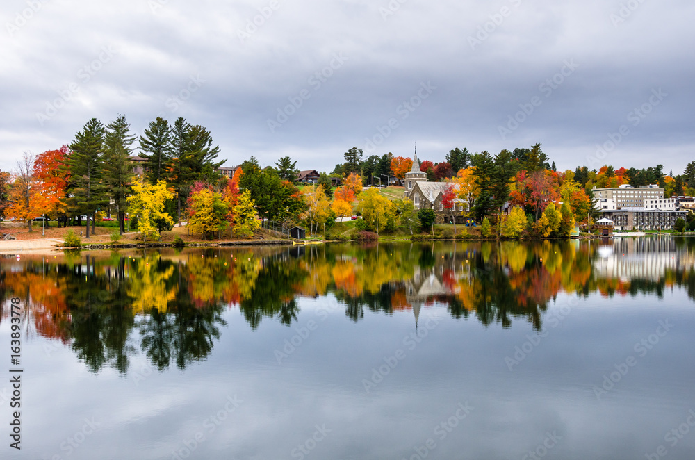 Buildings Among Colourful Trees and Reflection in Water ion a Cloudy Autumn Day. Lake Placid, NY.