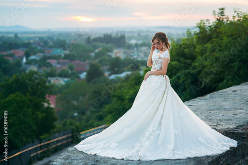 Young girl in wedding dress on city background at sunset.