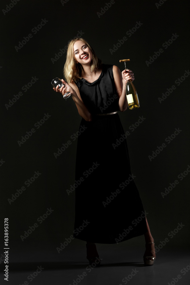 Beautiful drunk blonde woman holding white wine bottle on black background. Party and holiday