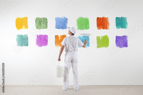 Rear view of painter man who make and chooses from various color samples isolated on the big blank white wall