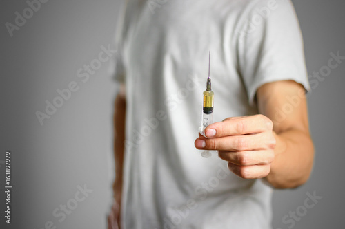 Wallpaper Mural A young man holding a syringe with a needle with the drug. Closeup. Isolated on a grey background Torontodigital.ca
