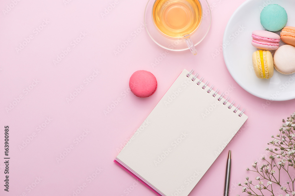 Flatlay of notebook, cake macaron, cup of tea and flower on pink table. Beautiful breakfast with macaroon. Flatlay of notebook, cake macaron, cup of tea and flower on pink table. Beautiful breakfast with macaroon.