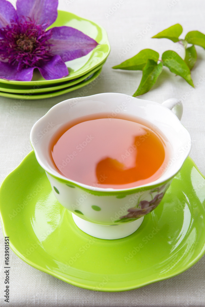 Tea in a cup of green and a bud of clematis colors in a rural style on a light background with a copy space Tea in a cup of green and a bud of clematis colors in a rural style on a light background with a copy space