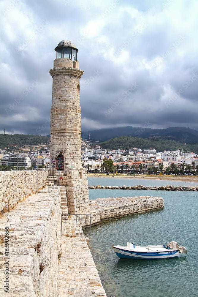 Stone pier, lighthouse and boat in the port of Chania. Crete