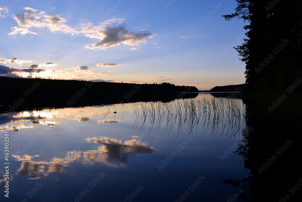 Sunset on summer night in central Finland. Calm lake with reflection, trees on the shores in shadows.