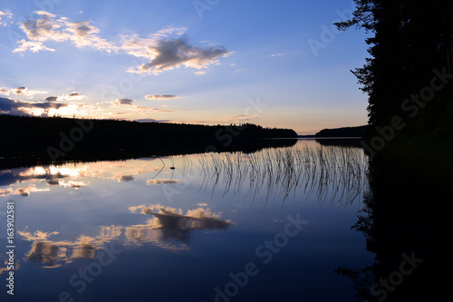 Sunset on summer night in central Finland. Calm lake with reflection, trees on the shores in shadows.
