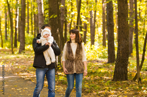Happy young family in the autumn park outdoors on a sunny day. Mother, father and their little baby boy are walking in the park. Love, family and parenthood concept.