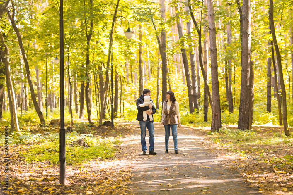 Obraz premium Happy young family in the autumn park outdoors on a sunny day. Mother, father and their little baby boy are walking in the park. Love, family and parenthood concept.