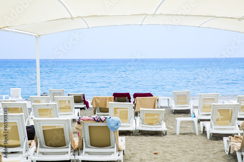 Fototapeta Naklejka Na Ścianę i Meble -  White plastic sunbeds in sandy beach under big parasol