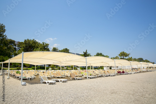 White plastic sunbeds in sandy beach under big parasol