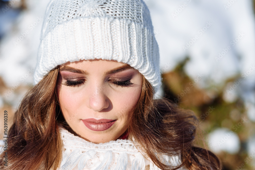 close up Winter portrait of a Happy candid beautiful young lady in a white knitted beanie hat and gloves close up Winter portrait of a Happy candid beautiful young lady in a white knitted beanie hat and gloves