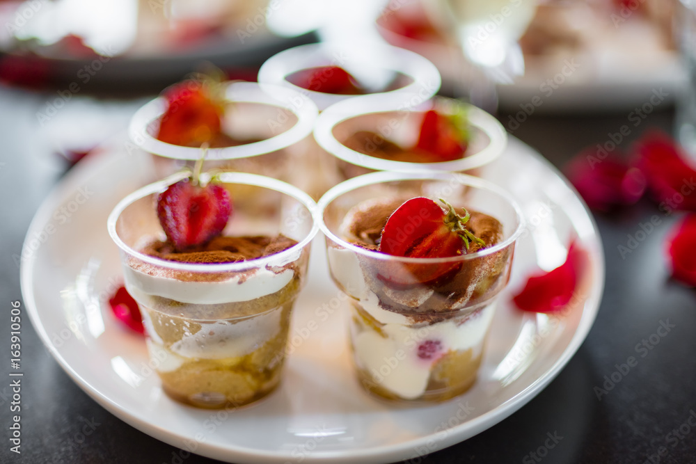 Delicious fresh cold strawberry cheese cake, dessert in plastic cups with rose petals on a dark background. Copy space Delicious fresh cold strawberry cheese cake, dessert in plastic cups with rose petals on a dark background. Copy space