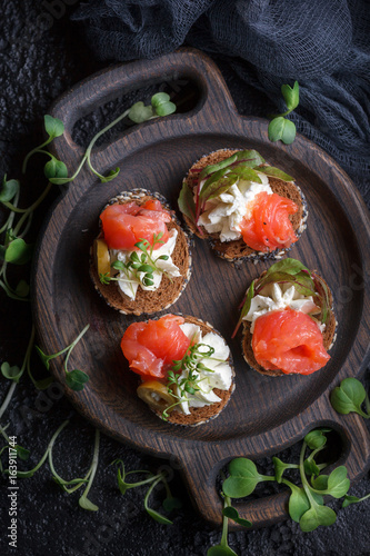 Delicious canape with salmon, cottage cheese, olive with micro greens on a dark background. Cold appetizer.