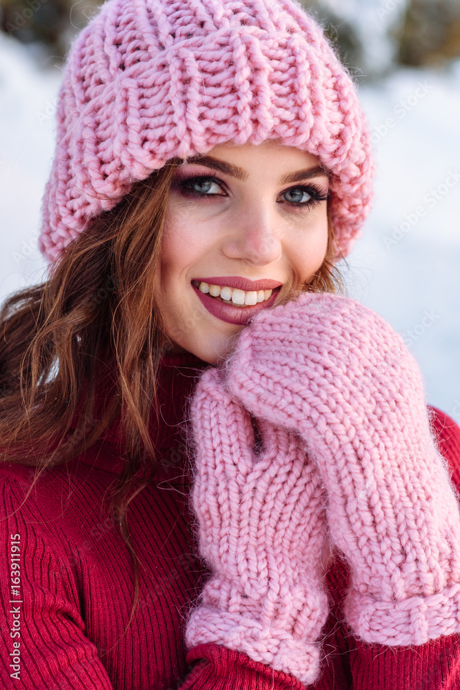 close up Winter portrait of a Happy candid beautiful young lady in a pink knitted beanie hat and gloves