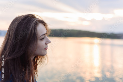 summer vacation happy portrait beautiful woman girl caucasian asian blended in blue shirt posing on background sky lake water sunset long hair brunette outdoors