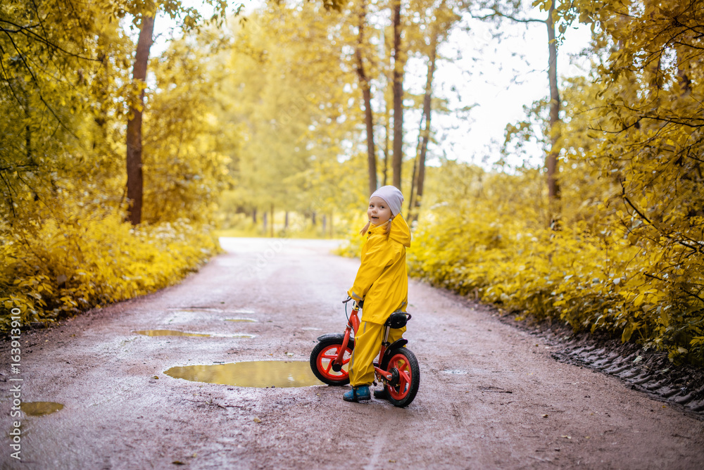 Little girl in yellow waterproof clothes with bike