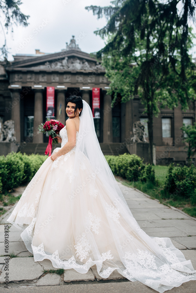 Beautiful bride with a burgundy bouquet in a magnificent wedding-dress