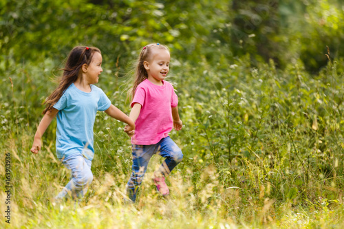 Two little girls running around holding hands in the park