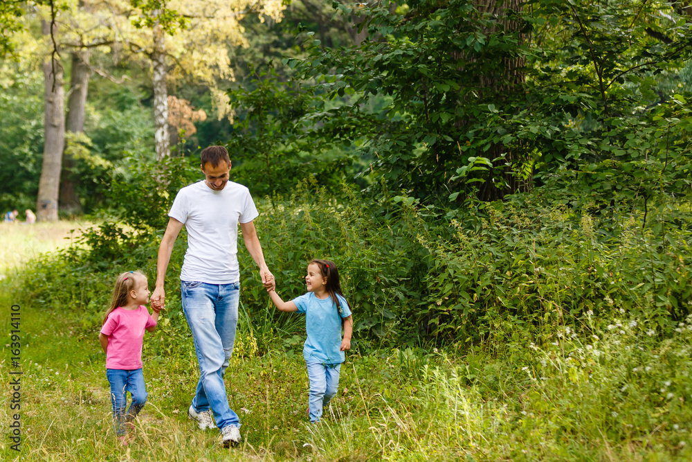 Father and two little daughters are walking in the park