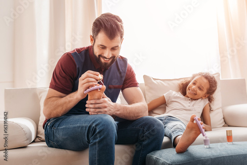 Happy father doing pedicure to cute little daughter at home