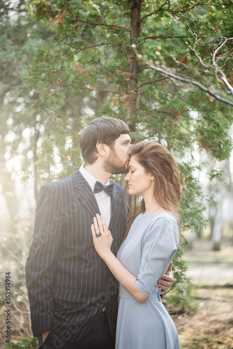 Beautiful young married couple kissing in the summer sunset park. Bride is wearing light blue dress and the groom has a beard © anastasianess