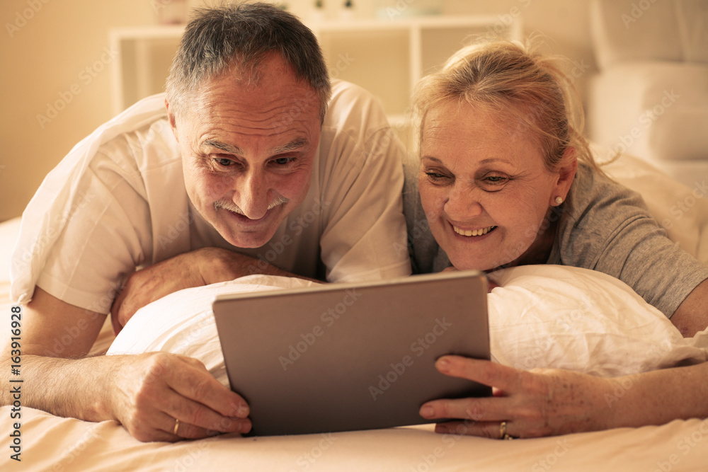 Senior couple using digital tablet in bed.