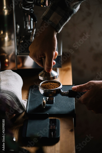 The process of making coffee step by step. Man tamping freshly ground coffee beans in a portafilter on a working wooden table photo
