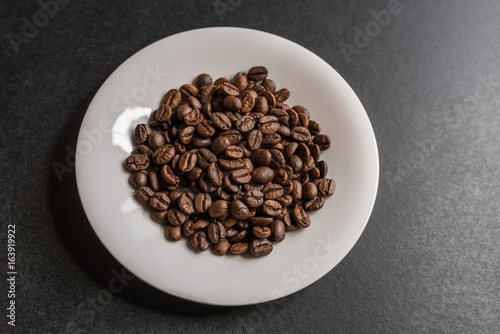 Roasted coffee beans in a white saucer on dark background. Selective focus.