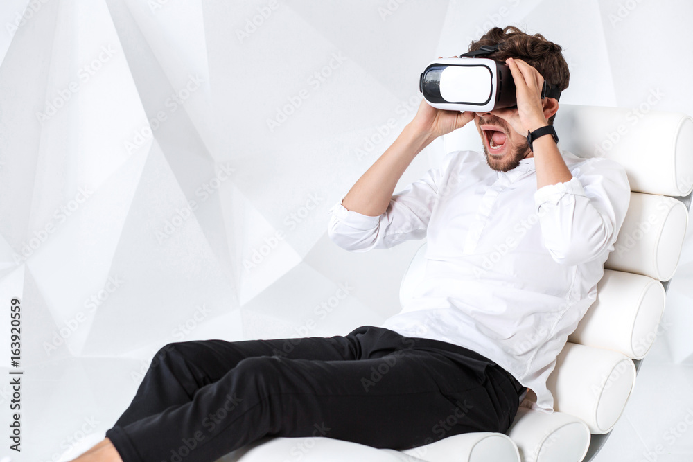 Excited young man is getting experience using VR-headset glasses of virtual reality gesticulating with his hands